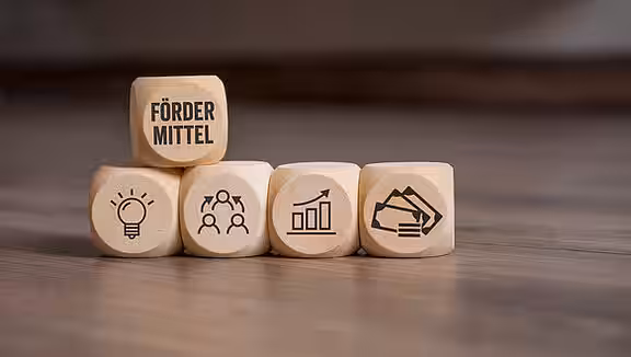 Gestapelte Spielwürfel; auf dem obersten steht "Fördermittel" geschrieben