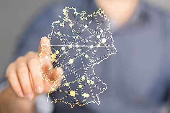 Im Vordergrund sind die Umrisse von Deutschland skizziert mit verschiedenen Netzwerkpunkten. Im Hintergrund zeigt ein Mann mit dem Zeigefinger auf einen Netzwerkpunkt.
