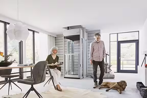 Ein älteres Ehepaar im Wohnbereich mit ihrem Hund mit einem Homelift im Hintergrund