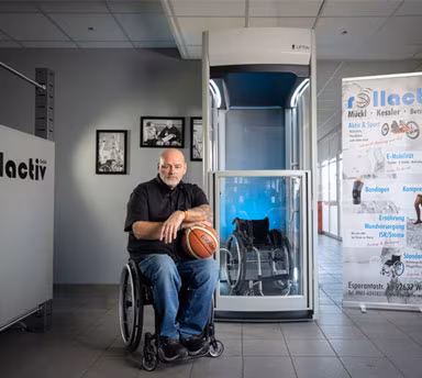 Mann sitzt im Rollstuhl mit einem Basketball in der Hand vor einem Homelift