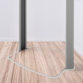 Ein Homelift steht still auf einem hellen Holzboden in einem modernen, weißen Raum. Zwei Metallsäulen und eine Markierung auf dem Boden kennzeichnen den Aufstellbereich des Homelifts.